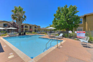 Exterior pool, covered picnic tables, lounge chairs, surrounding landscaping, railing and steps leading into pool.