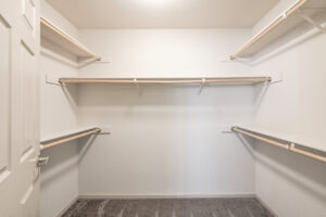 Interior unit walk-in closet, 5 shelves, 5 hanging racks, gray carpeting in walk-in closet, white walls.